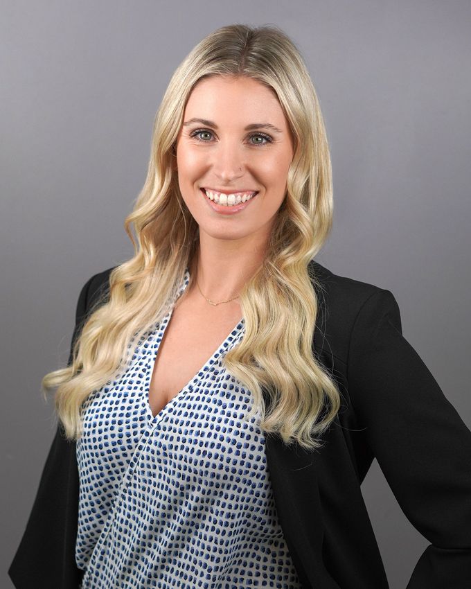 A woman wearing a black jacket and a blue shirt is smiling for the camera.