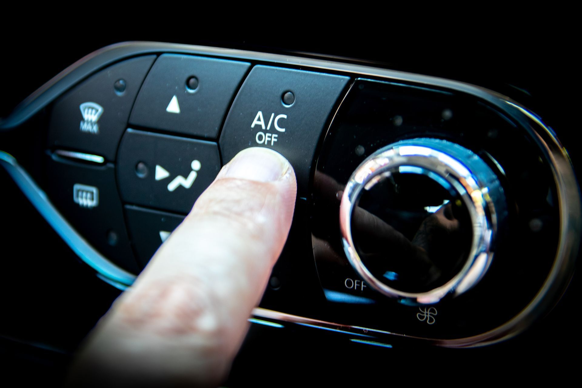 Finger pressing A/C button on a car dashboard climate control panel.