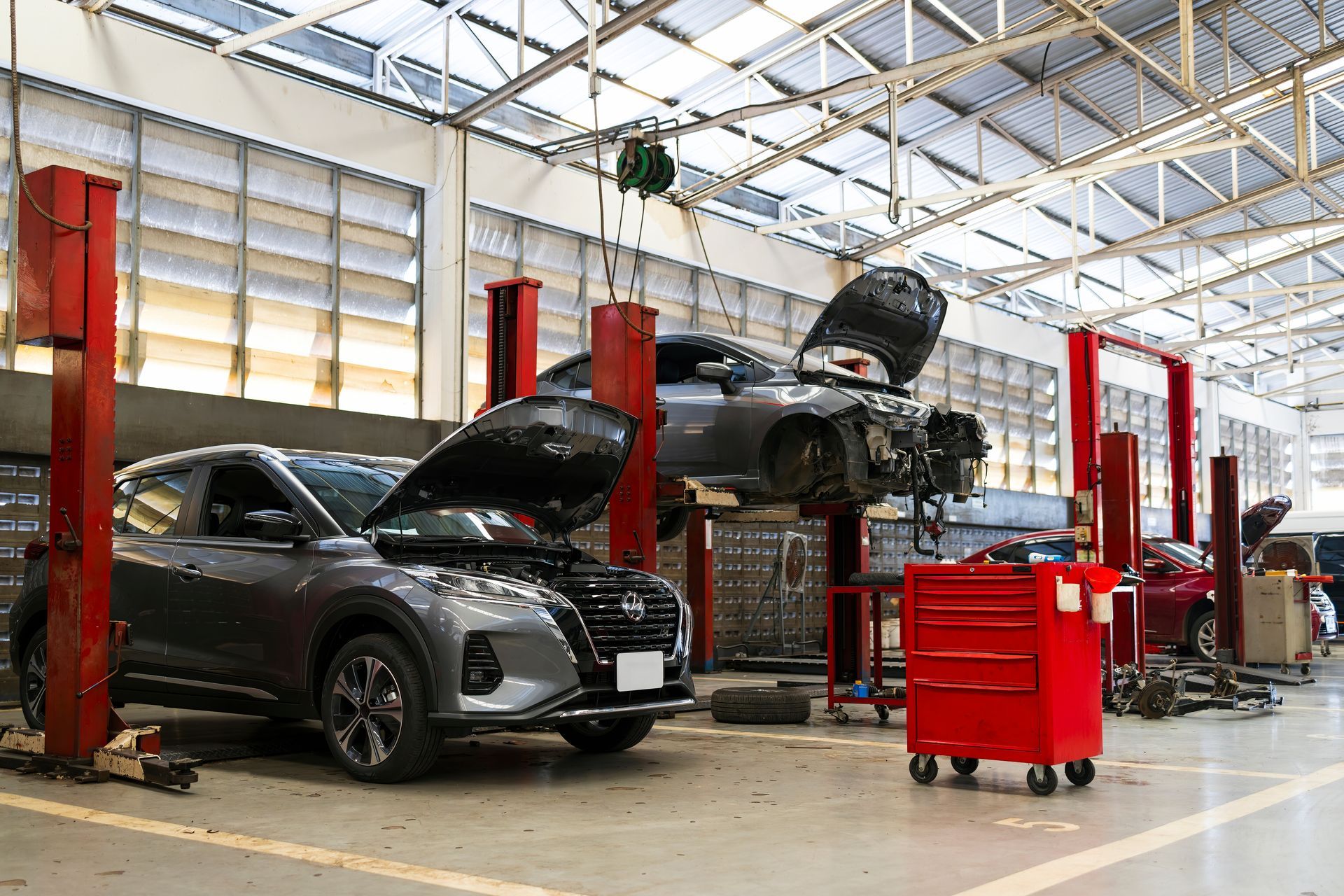 Cars in an auto repair garage with hoods open and a red tool chest nearby