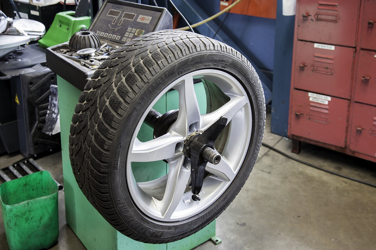 Car wheel with tire suspended in a workshop, near tools and red storage drawers.
