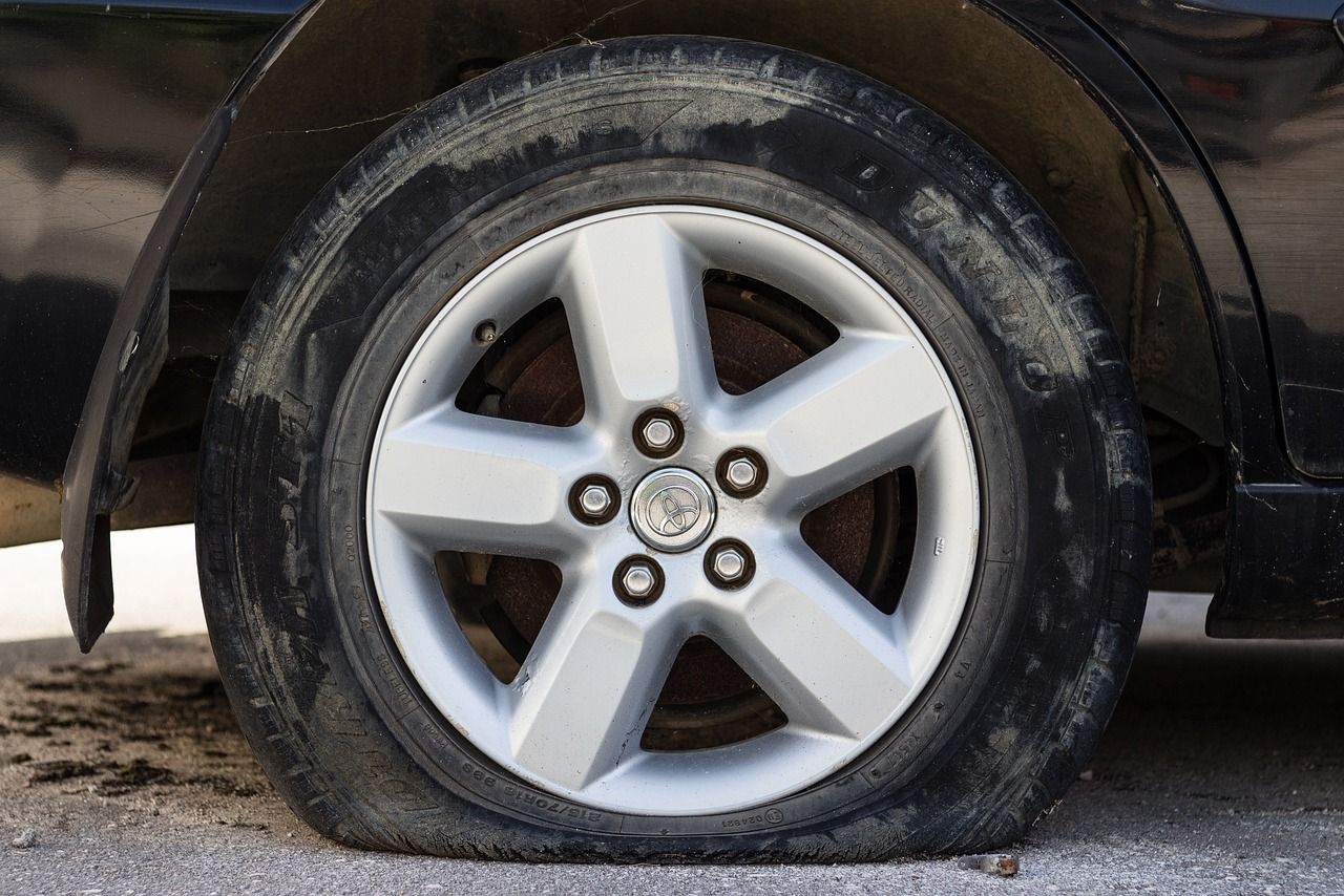 Flat tire on a dark car, with the wheel rim resting on the ground.
