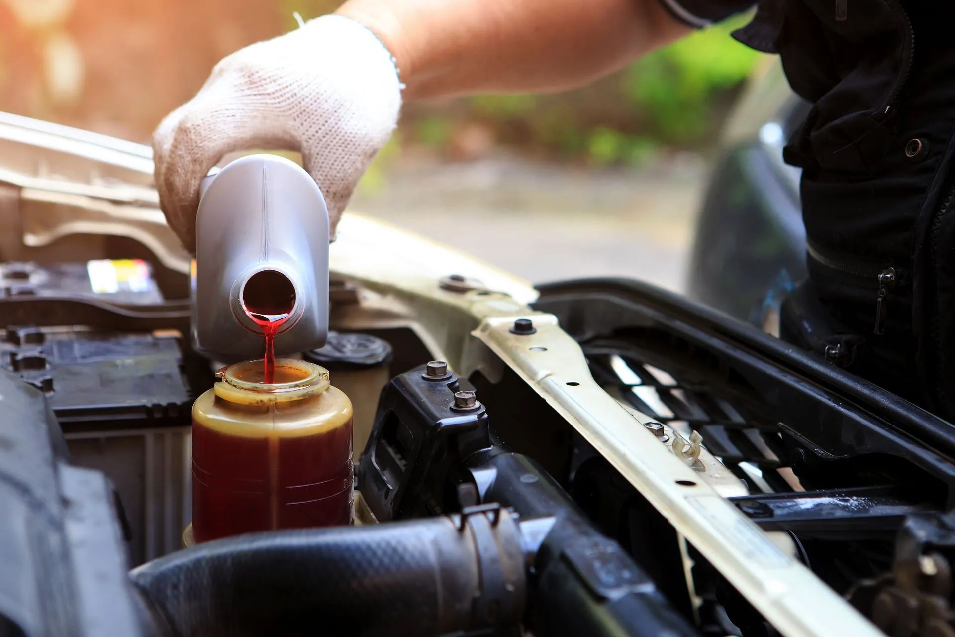 Mechanic pouring red fluid into a car reservoir under the hood
