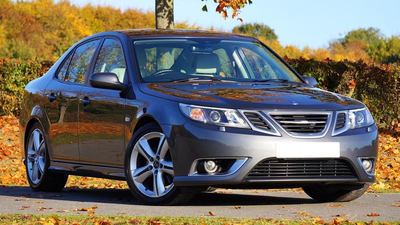 Blue sedan parked on a road with autumn trees in the background