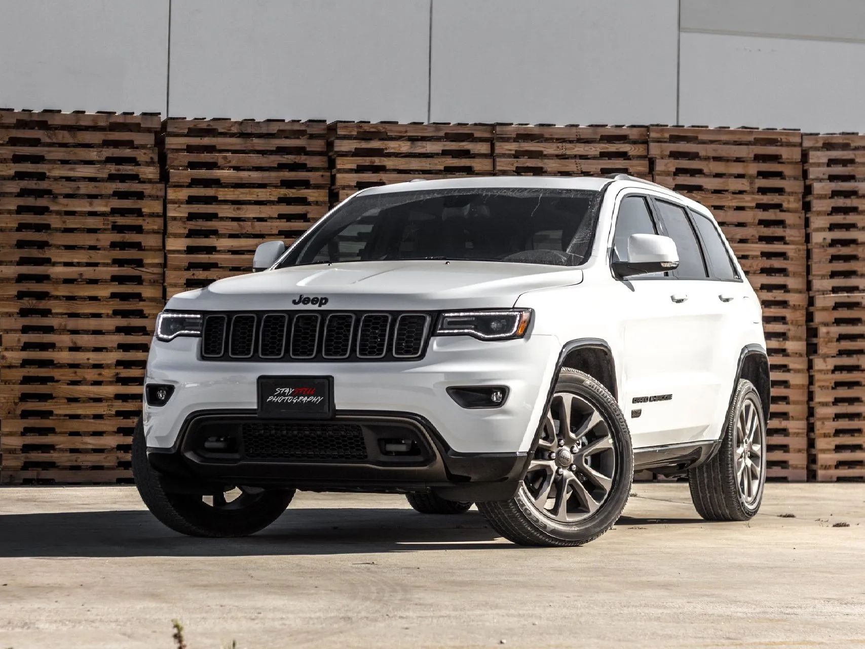 White Jeep SUV parked on concrete in front of stacked wooden pallets