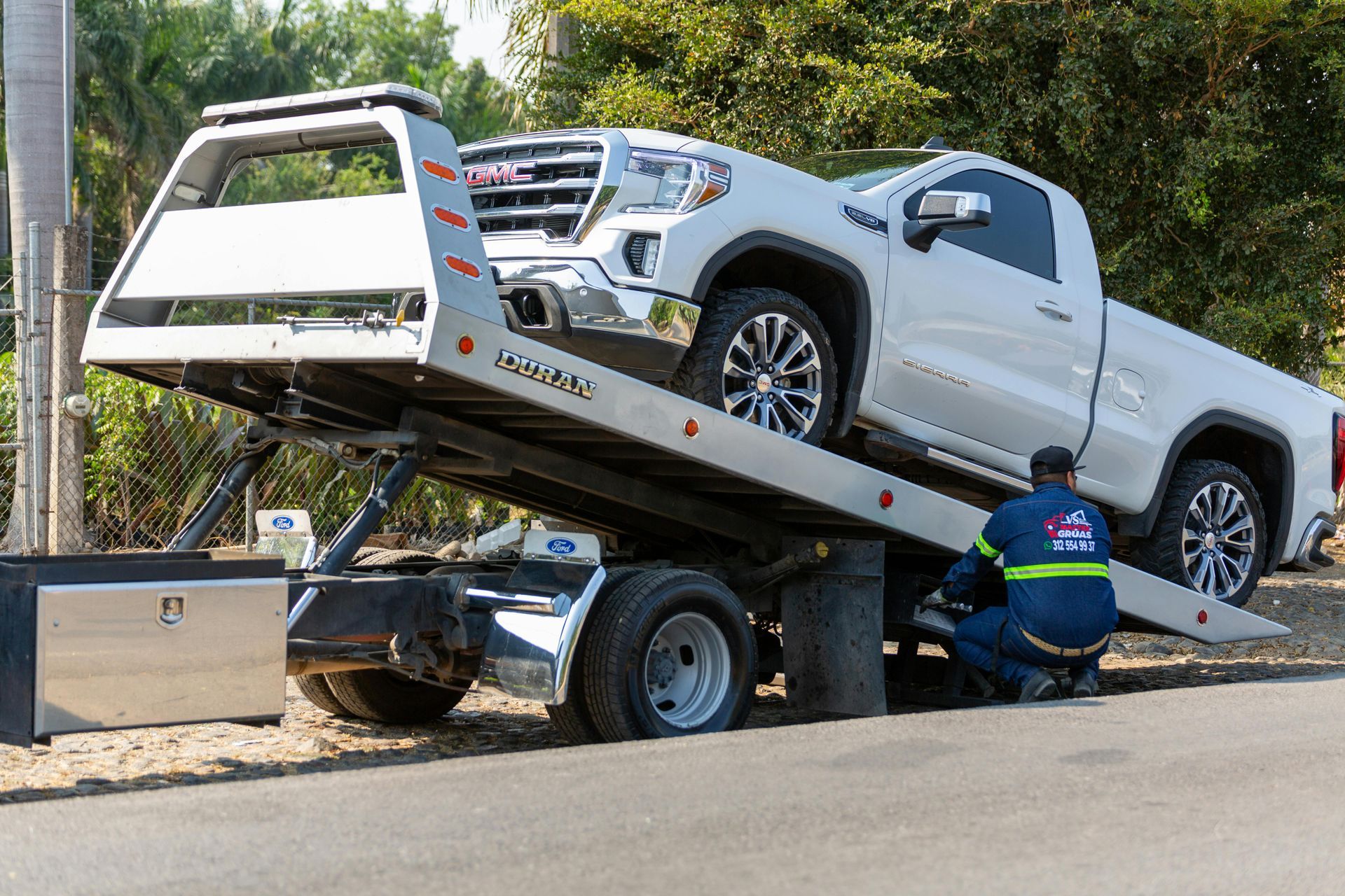 Tow truck loading a white pickup truck onto a flatbed on a roadside