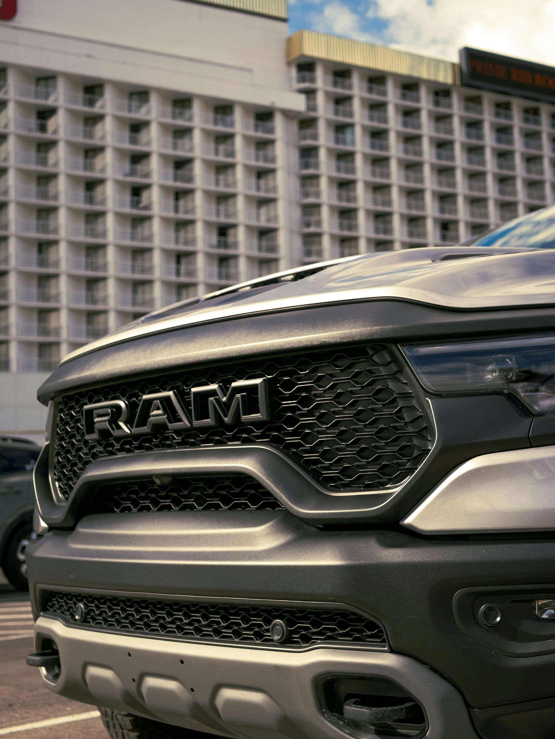 Front grille of a gray RAM pickup truck parked outdoors in front of a building
