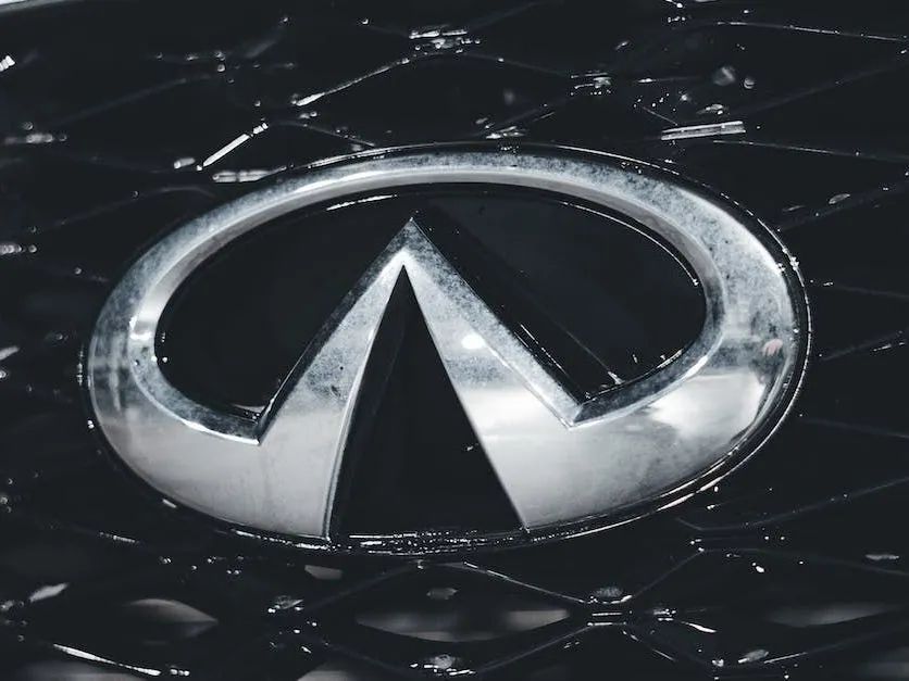 Silver Infiniti logo on a black car hood with reflections and light scratches