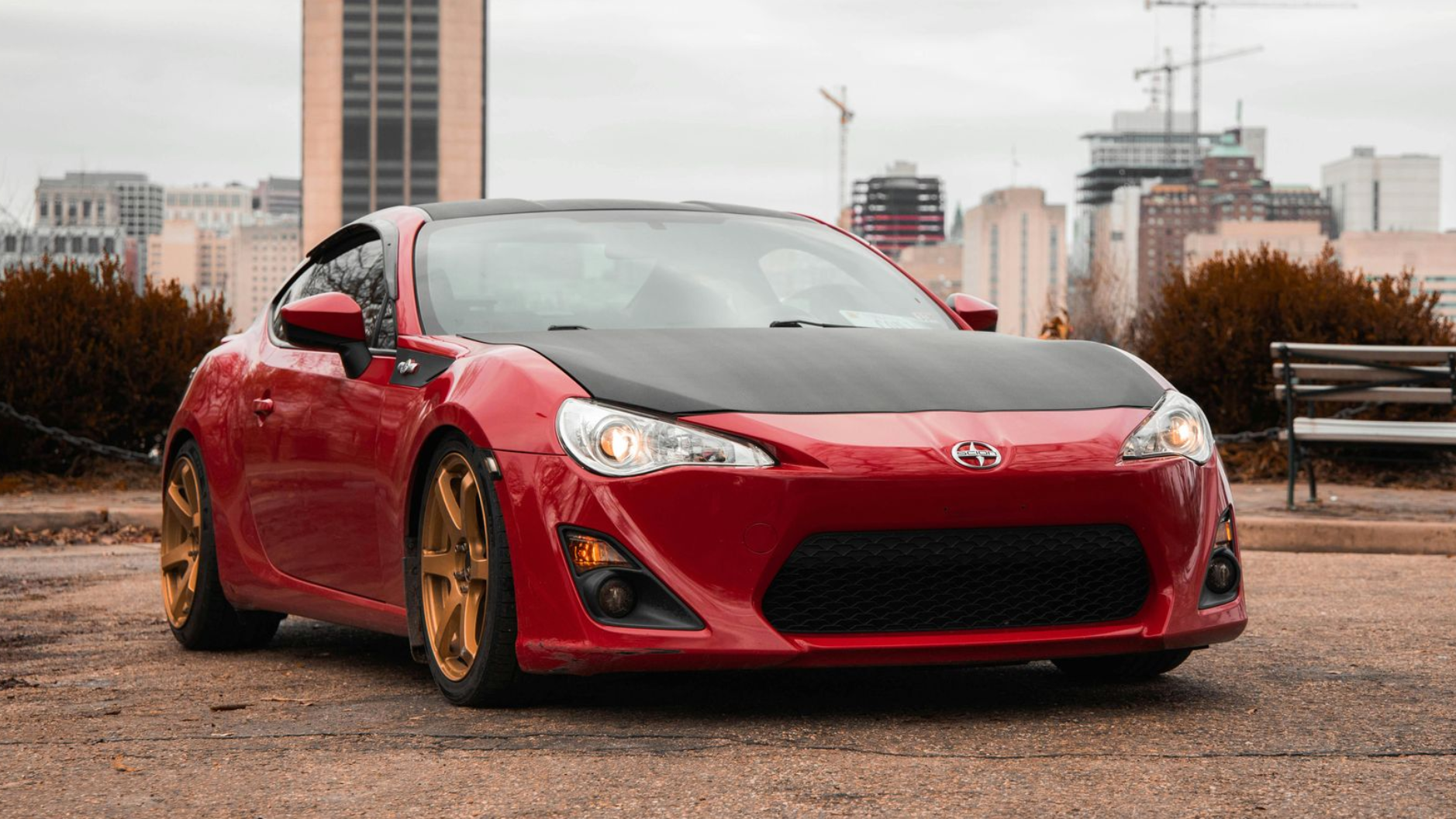 Red sports coupe parked on a wet street with city buildings in the background