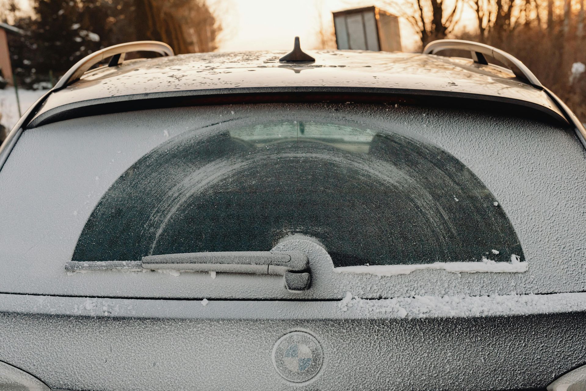 Snow-covered car rear window and hatchback parked outdoors in winter.