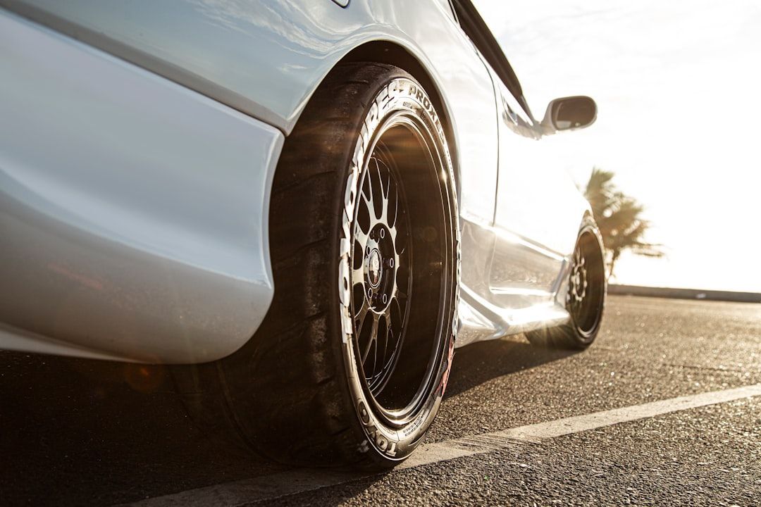 White sports car parked on a sunlit road, close-up of the rear wheel and side panel