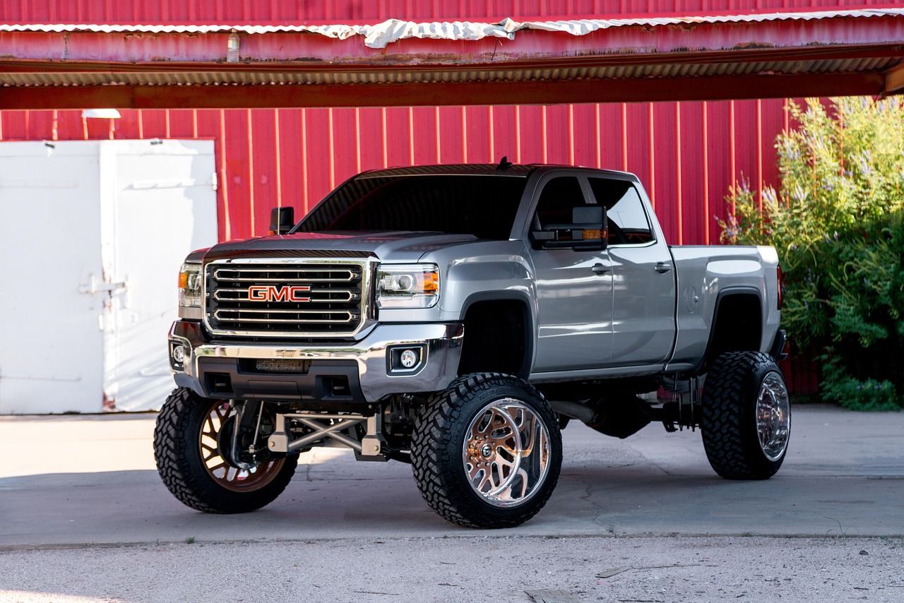 Gray GMC pickup truck with lifted suspension parked in front of a red barn building