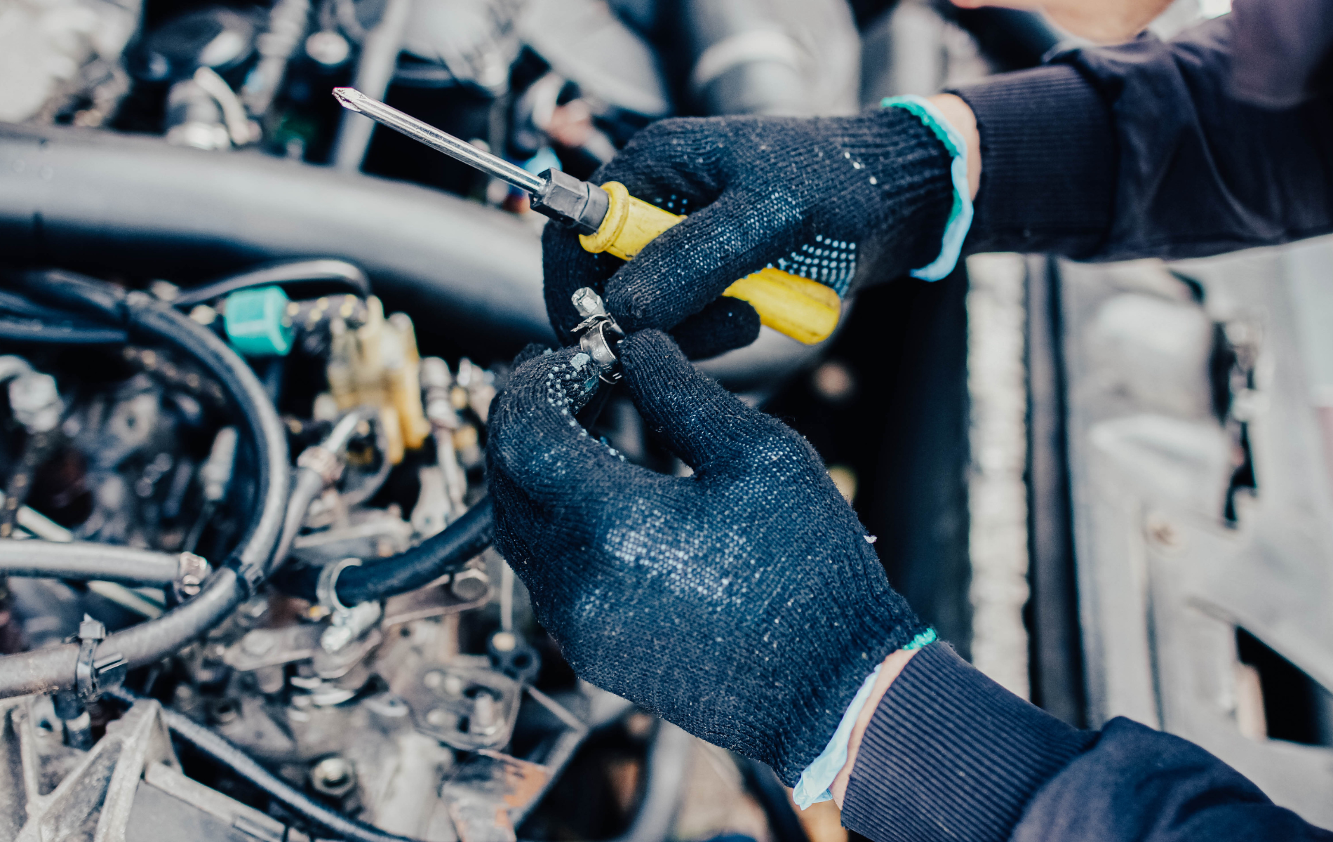 A man is working on a car engine with a screwdriver.