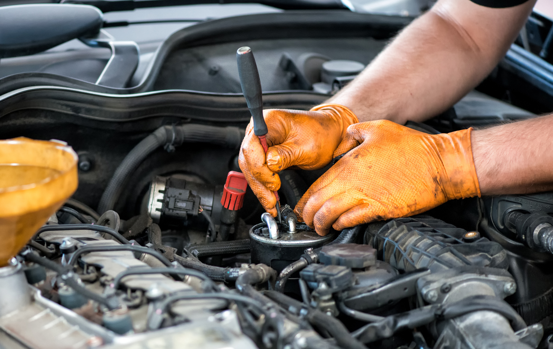 A man wearing orange gloves is working on the engine of a car.