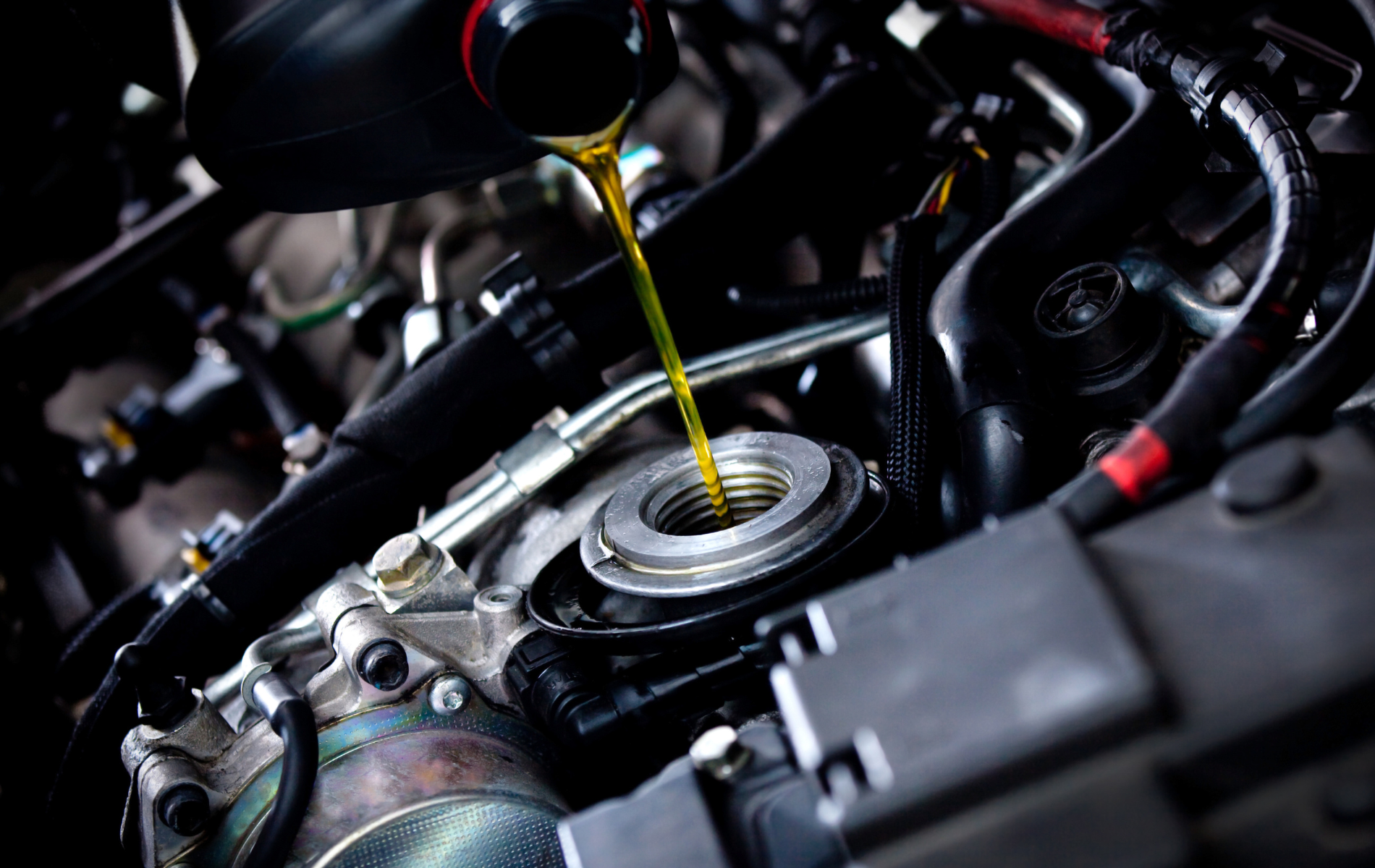 A close up of a person pouring oil into a car engine.