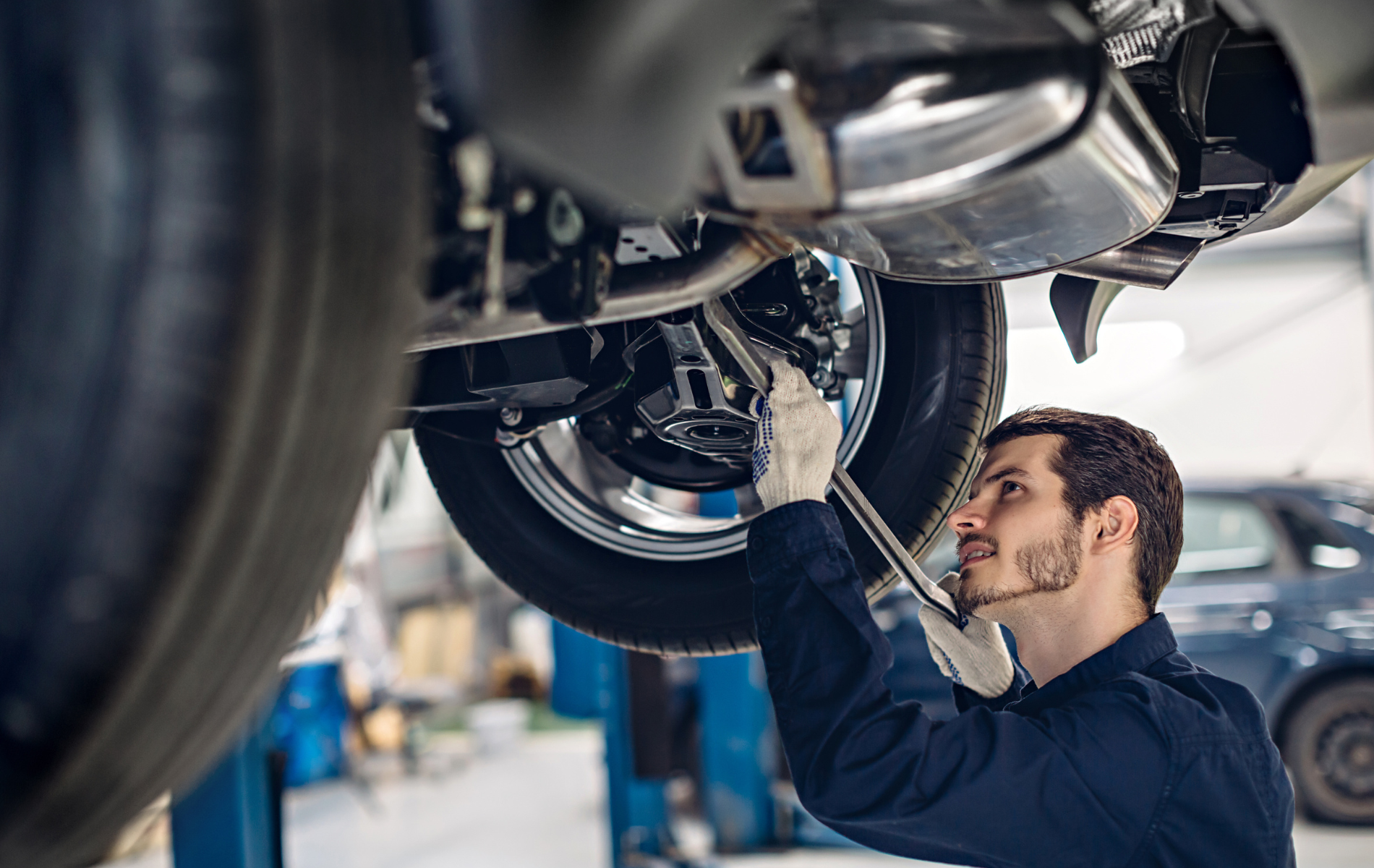 A man is working on the underside of a car in a garage.