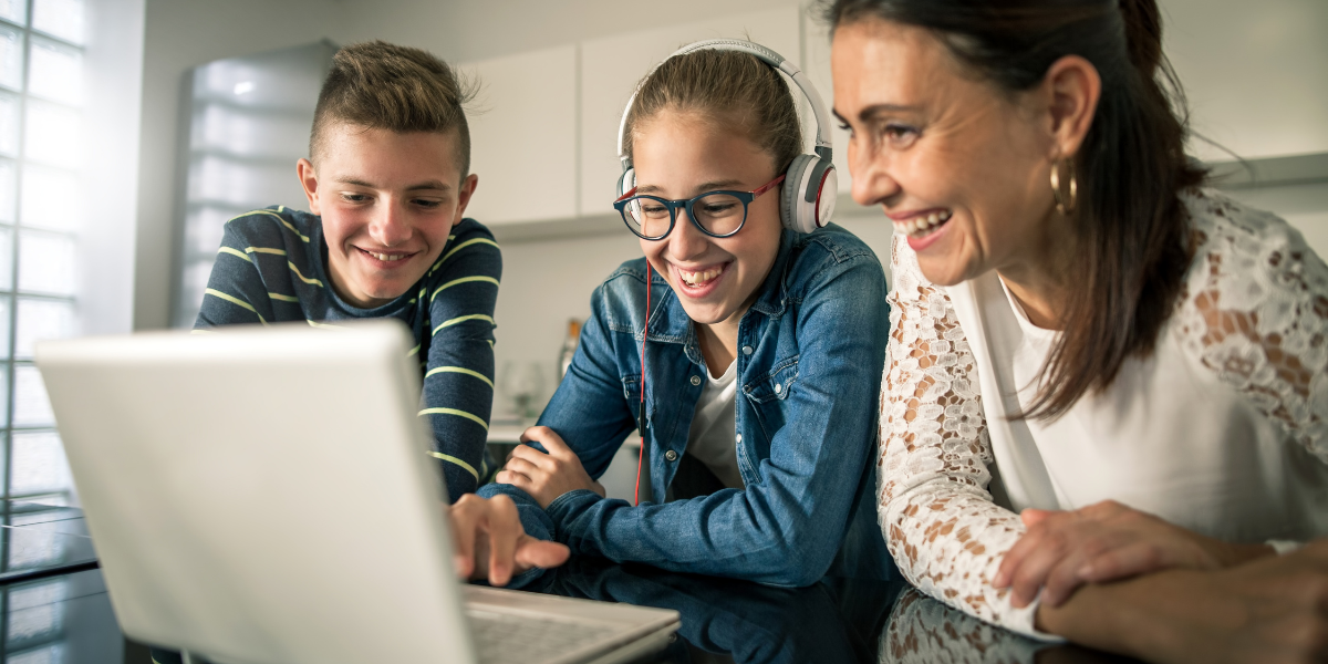 Mom with kids smiling while looking at a laptop during online school.
