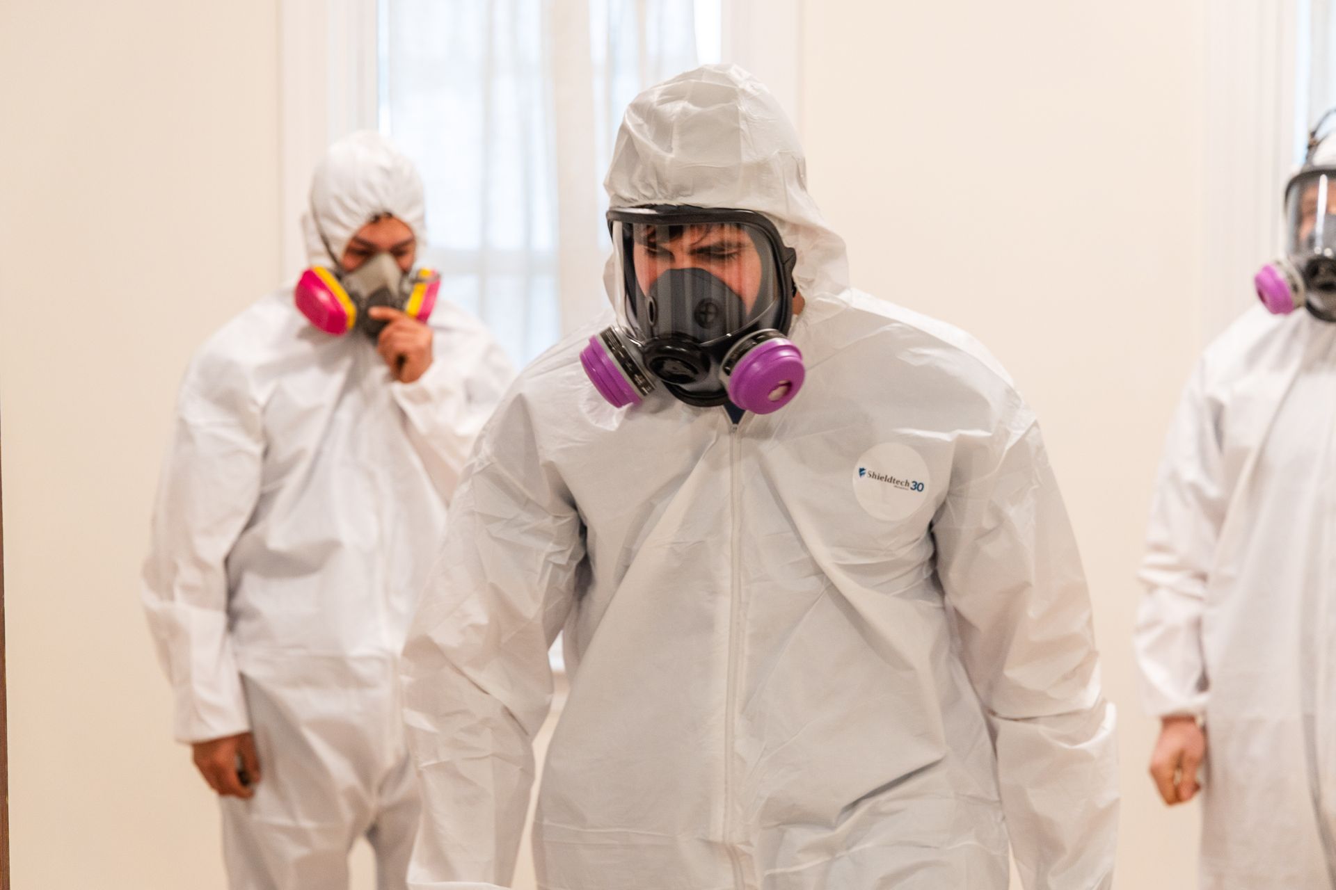 People in white hazmat suits and respirators walking in a clean corridor