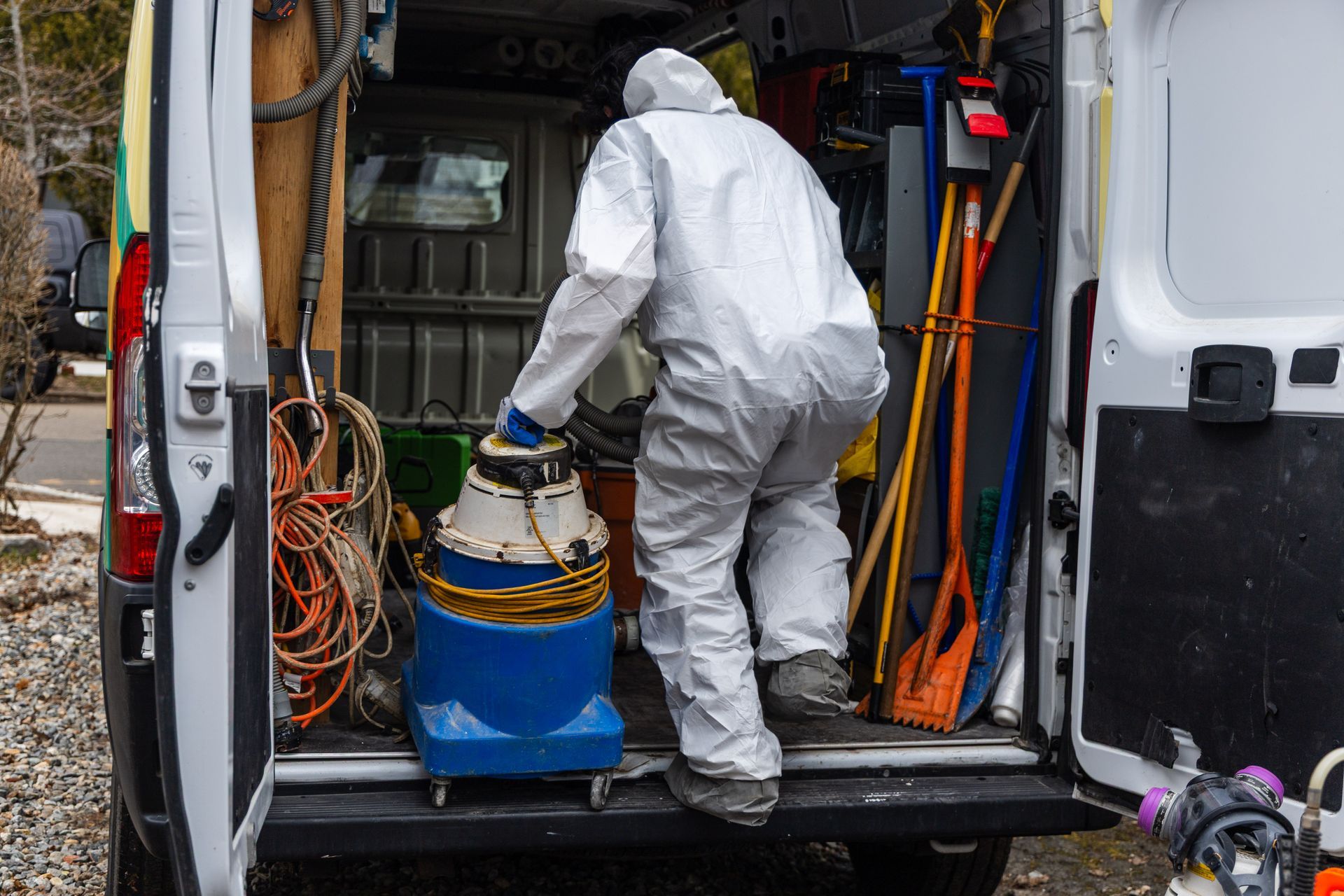Person in white protective suit handling equipment in the back of a van full of tools and hoses