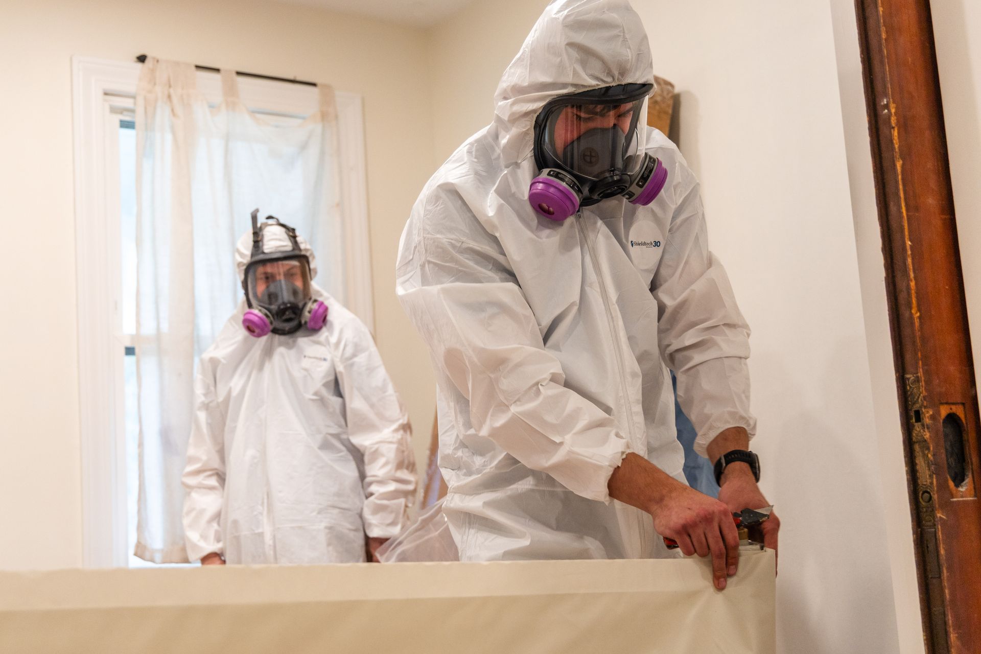 Two workers in white protective suits and respirators inspecting a room under renovation.