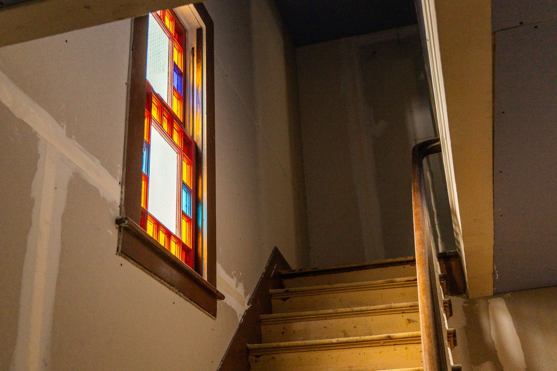 Staircase landing with wooden steps and a colorful stained-glass window on the left wall.