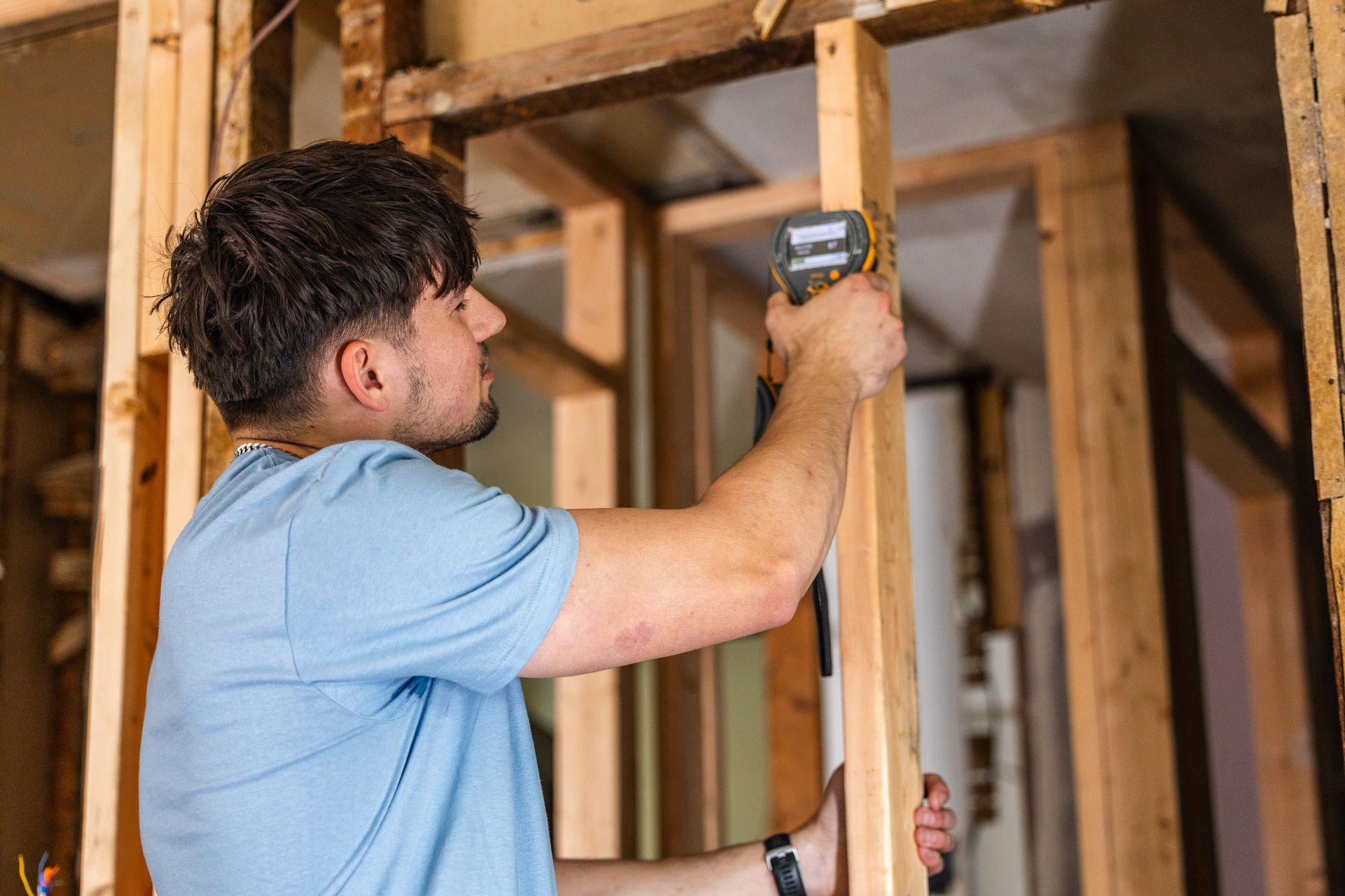 Person in a light blue shirt measures wooden framing with a tape measure inside a construction site