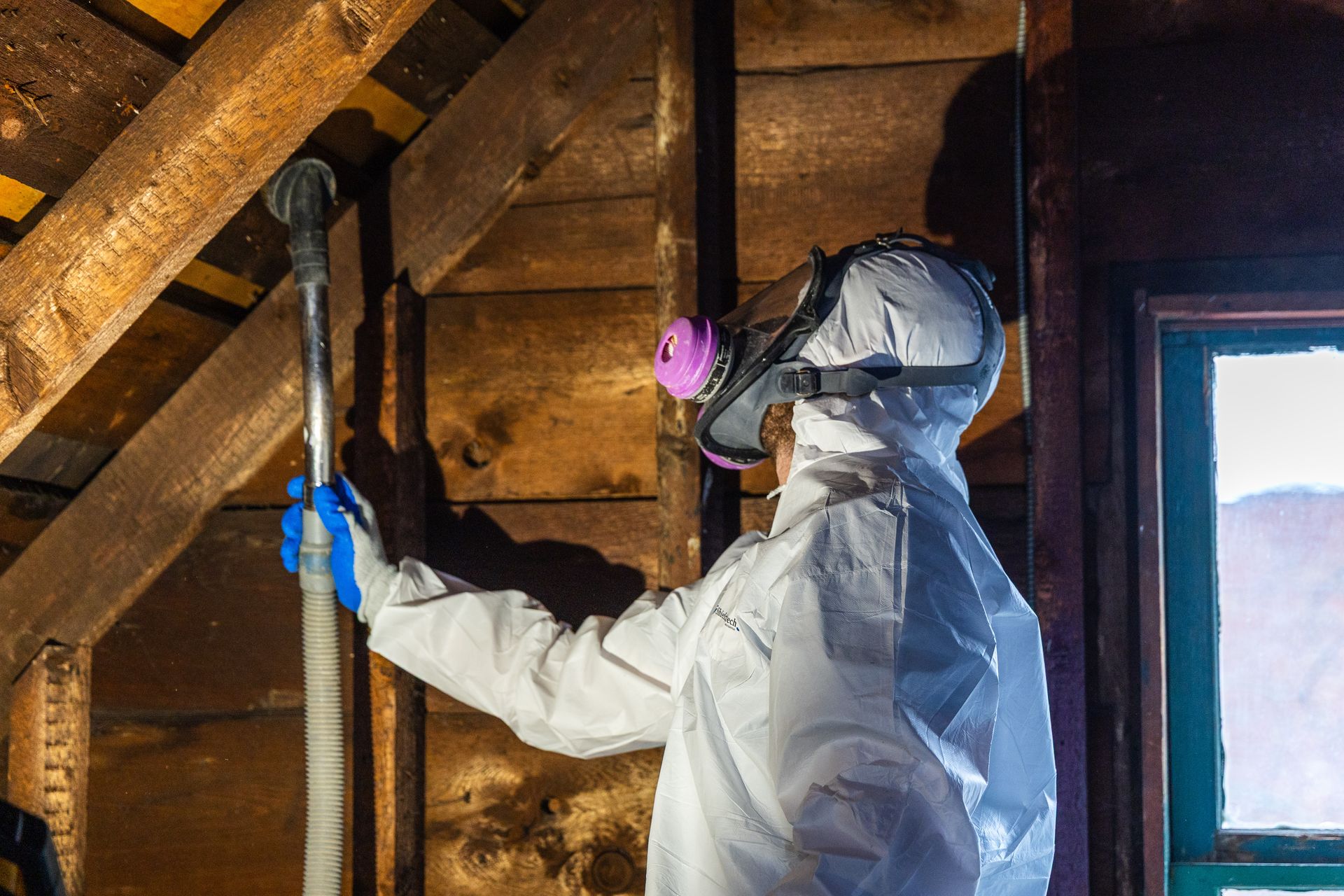 Worker in protective gear spraying a wooden attic wall with a spray gun