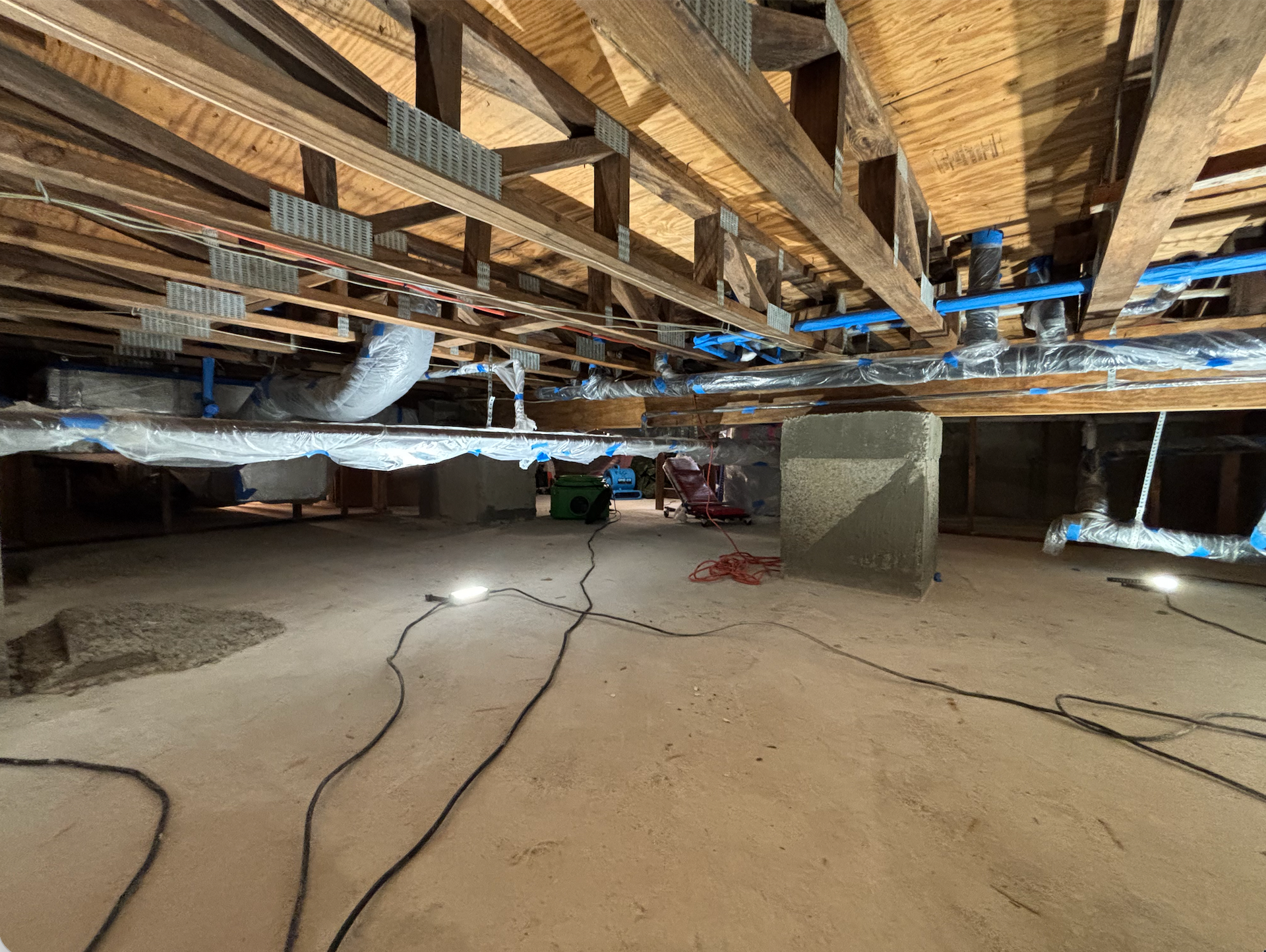 Unfinished basement with exposed wooden beams, ducts, and electrical wires on a concrete floor