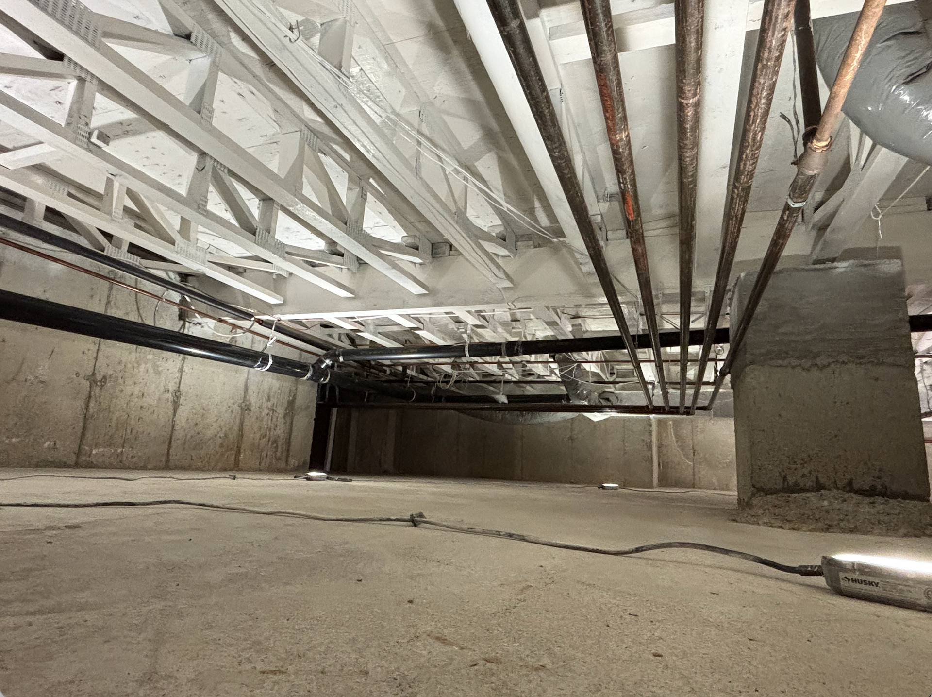Concrete basement with exposed ceiling beams, pipes, and unfinished walls.