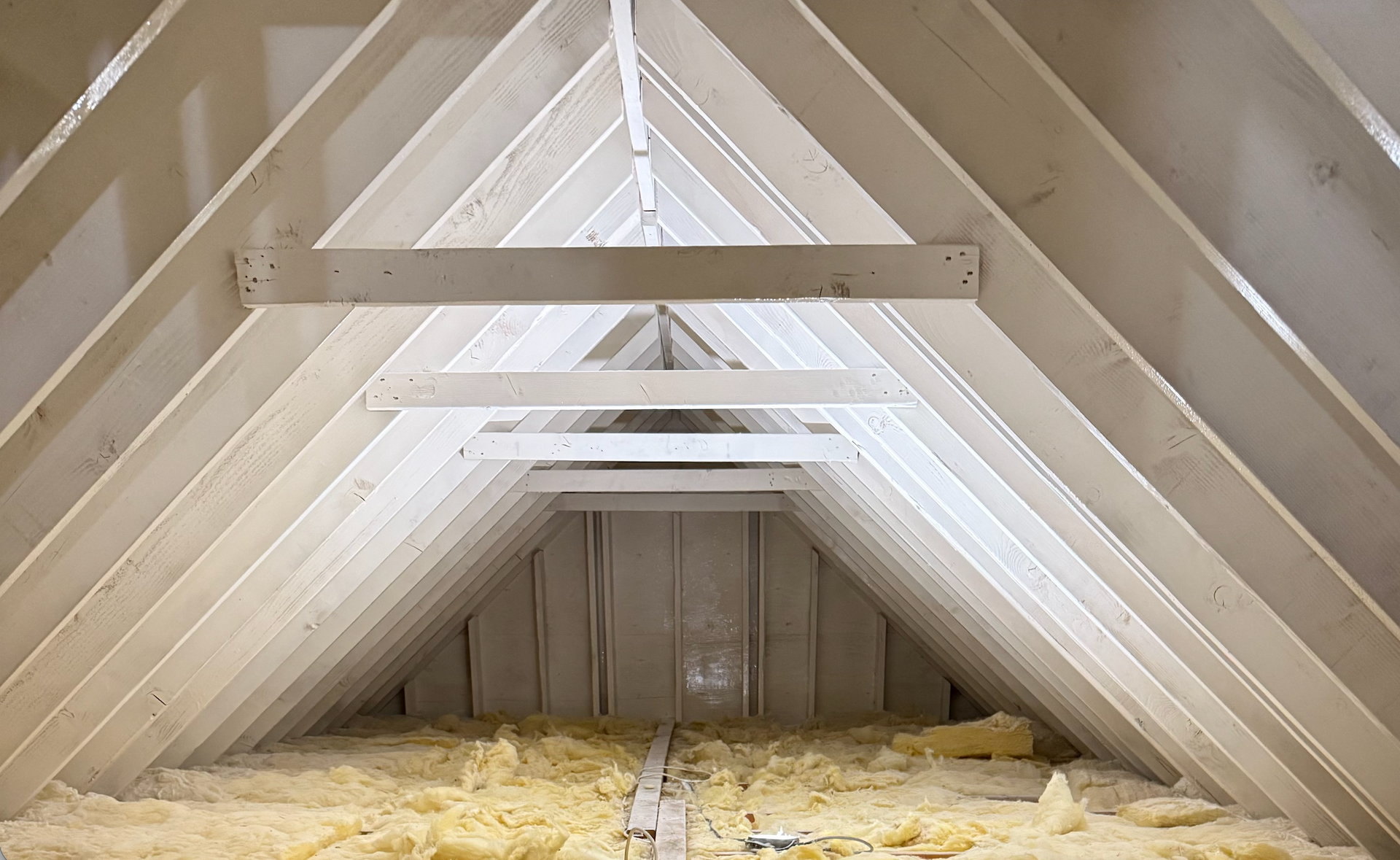 Empty attic interior with exposed white rafters and insulation on the floor