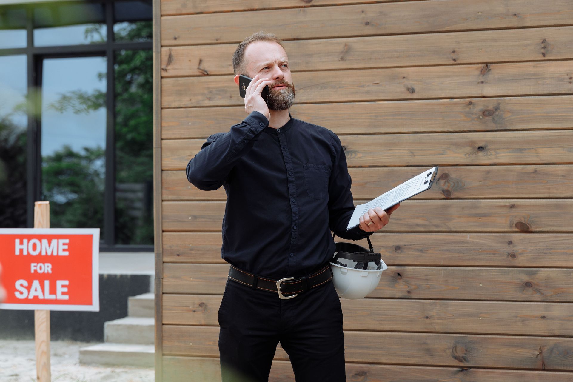 Real estate agent on phone beside a house with a red 