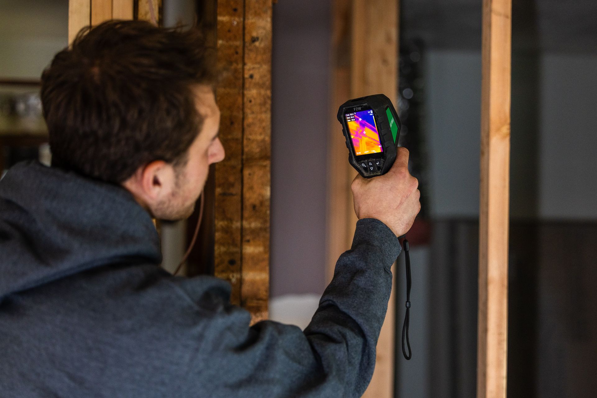 Person using a thermal camera to inspect an interior wall stud frame.