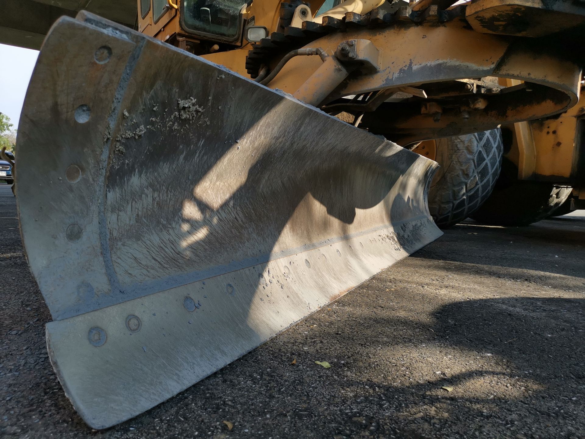 Bulldozer blade, close up, covered in dirt, on asphalt.