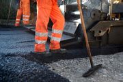 Workers in orange workwear paving a road with asphalt.