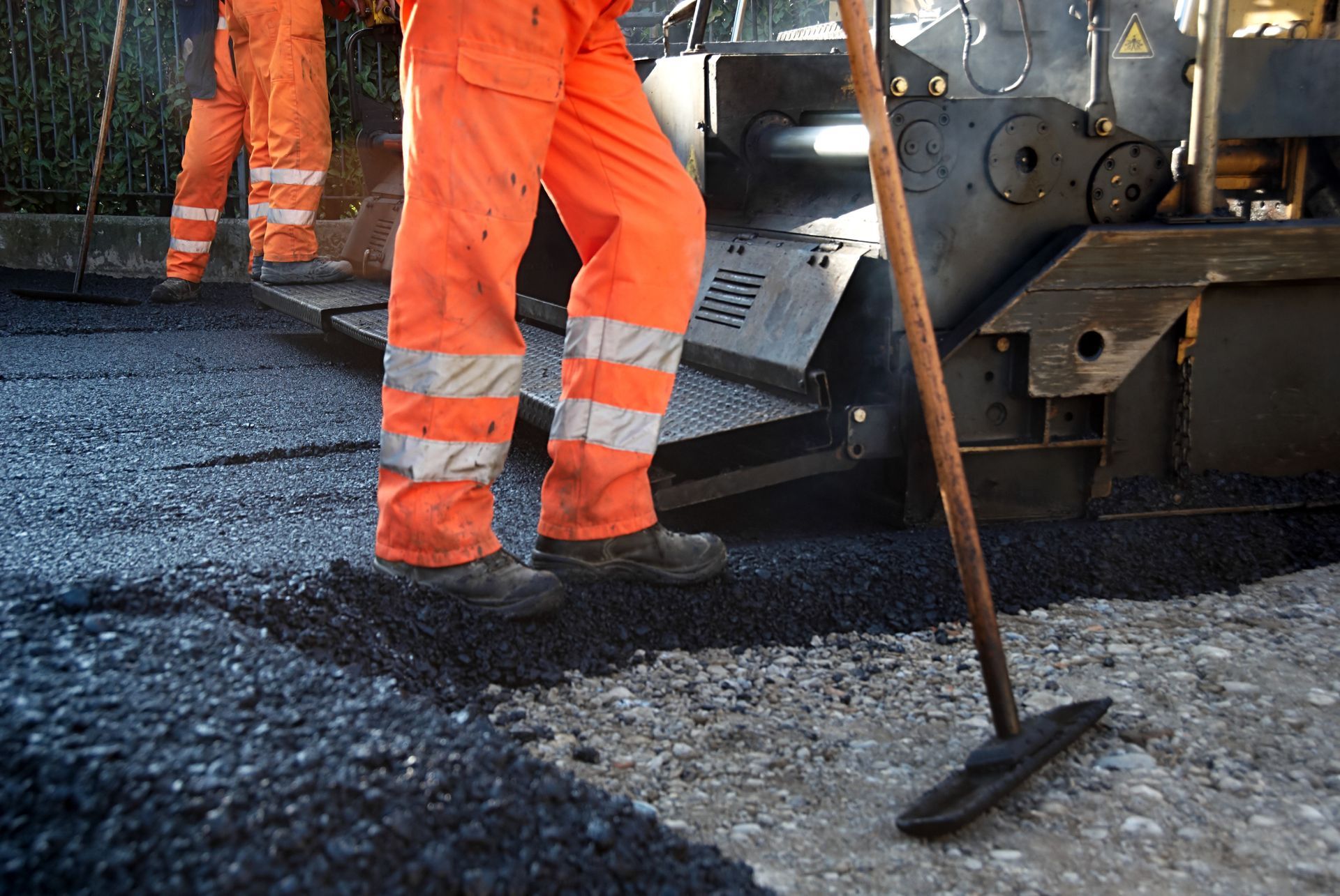 Workers in orange workwear paving a road with asphalt.