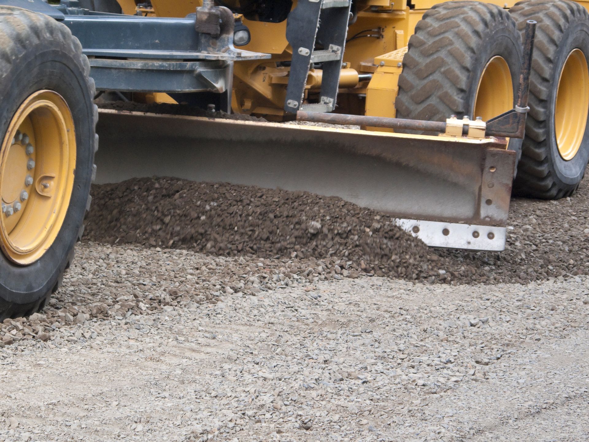 Road grader blade smoothing gravel road surface.