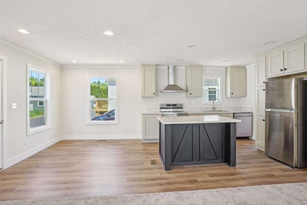 Bright kitchen with wood floors, white cabinets, gray island, stainless steel appliances, and windows.