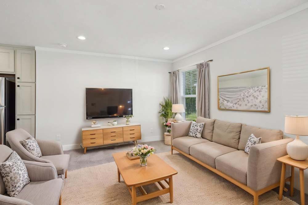 Living room with neutral tones: sofa, armchairs, TV, wooden furniture, window, and art.