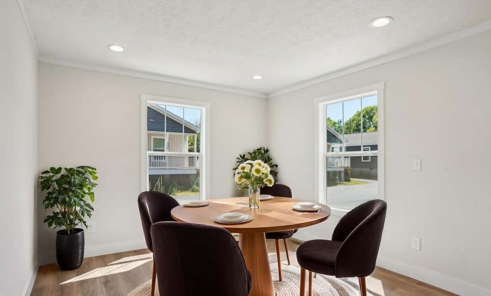Dining room with round table, dark chairs, and two windows.