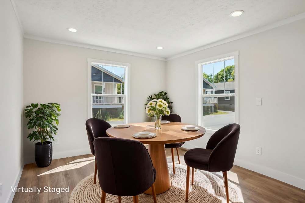 Dining room with round wooden table, four dark chairs, and two windows.