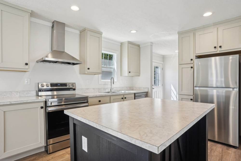 A modern kitchen with light gray cabinets, stainless steel appliances, and a dark gray island.