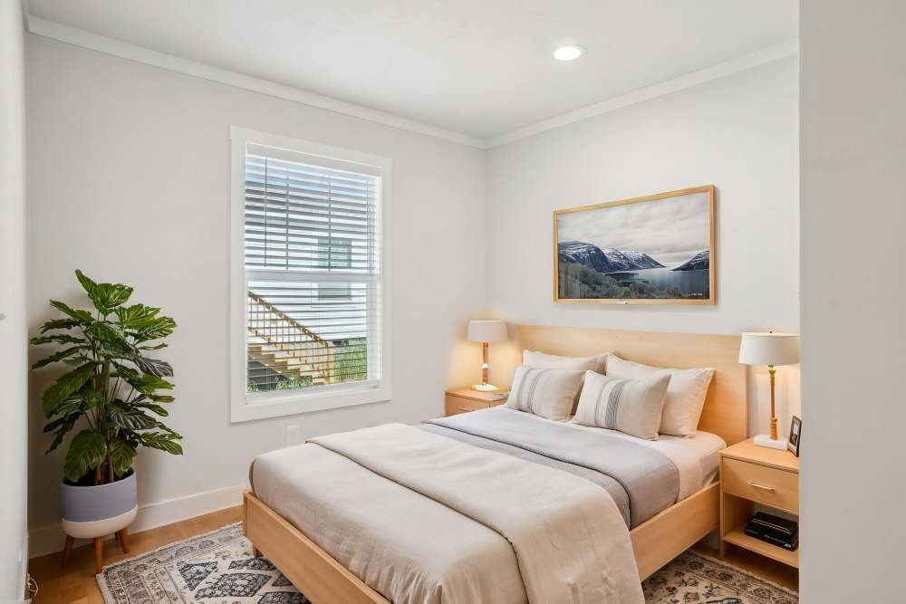 Bedroom with wooden bed, nightstands, landscape art, and a window with blinds.