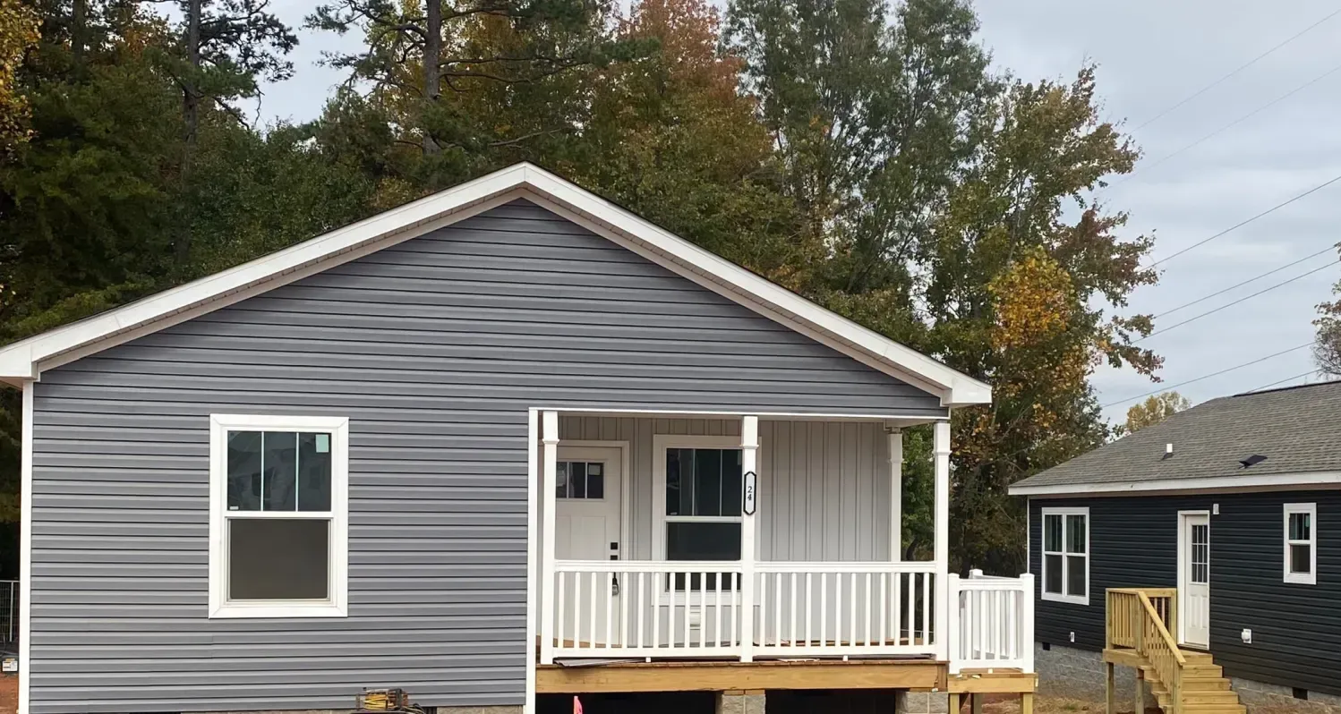 Two small houses with gray siding and white trim, surrounded by fall trees.