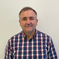 A man in a plaid shirt is standing in front of a white wall.