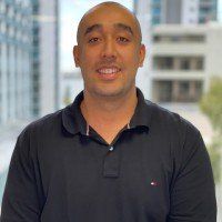 A bald man wearing a black polo shirt is smiling for the camera.