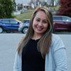 A woman is smiling in a parking lot with cars parked in the background.