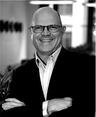 A man wearing glasses and a suit is smiling in a black and white photo.