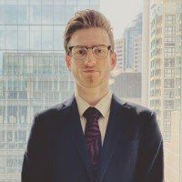 A man in a suit and tie is standing in front of a window.