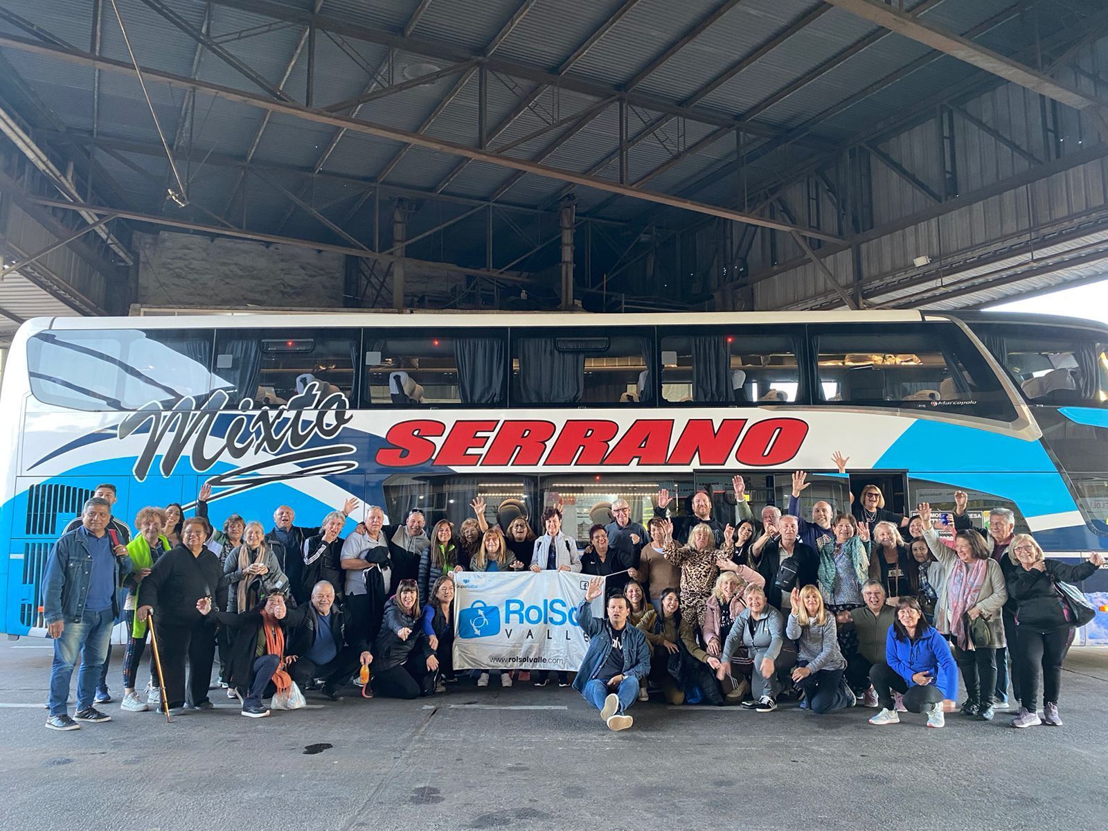 Gran grupo posando frente a un autobús turístico azul y blanco con