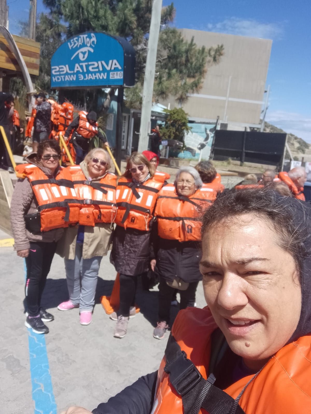 Grupo de personas con chalecos salvavidas de color naranja, cerca de un edificio con señalización.