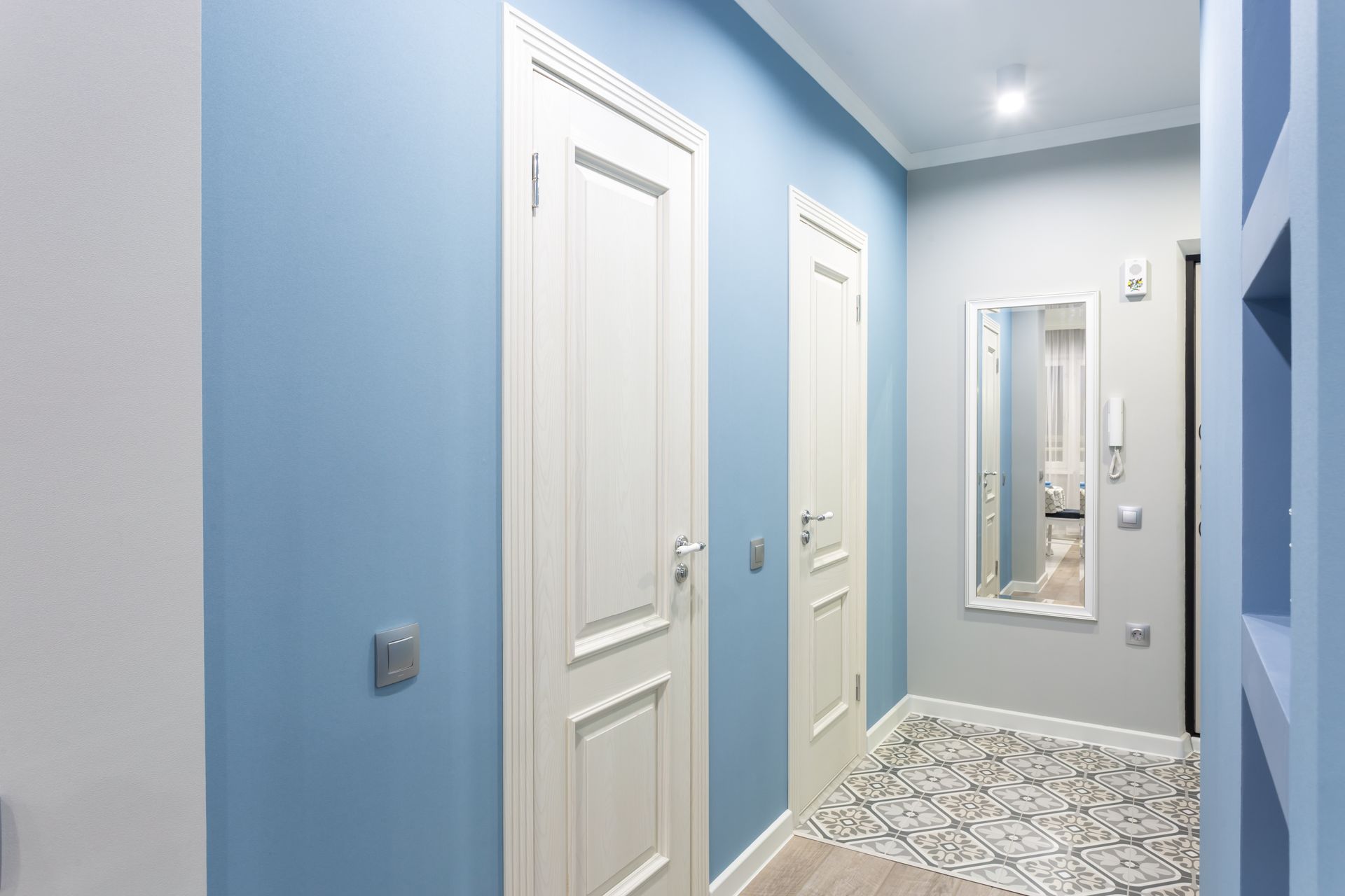 A hallway with blue walls and white doors and a mirror.